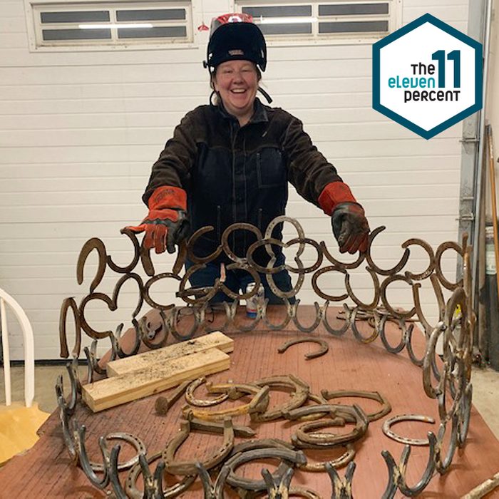 portrait of Brenda Hay in a garage standing behind a welded project