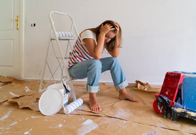 Stressed woman sits in bedroom renovation with paint mess around her in the floor