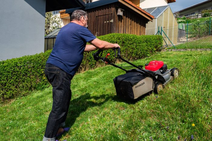 A man mowing the lawn in his yard with a Honda HRX76 lawn mower.