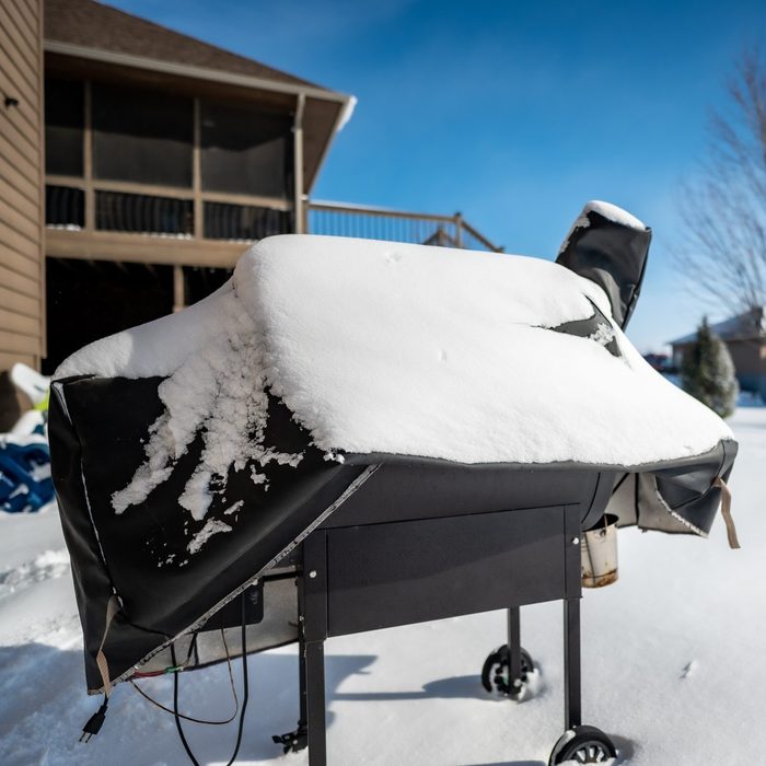 Snow covered BBQ smoker grill in the backyard in winter